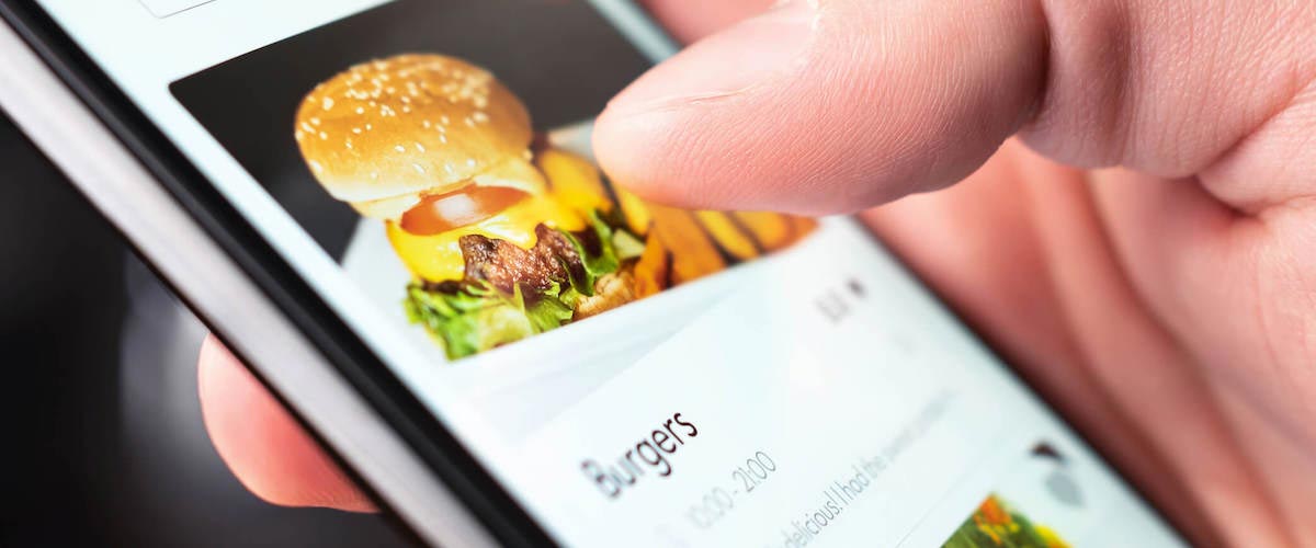 Hand on smartphone ordering burgers on mobile interface from ghost kitchen using local content