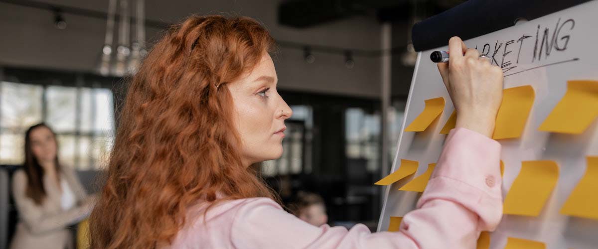 red haired woman writing on whiteboard with orange sticky notes