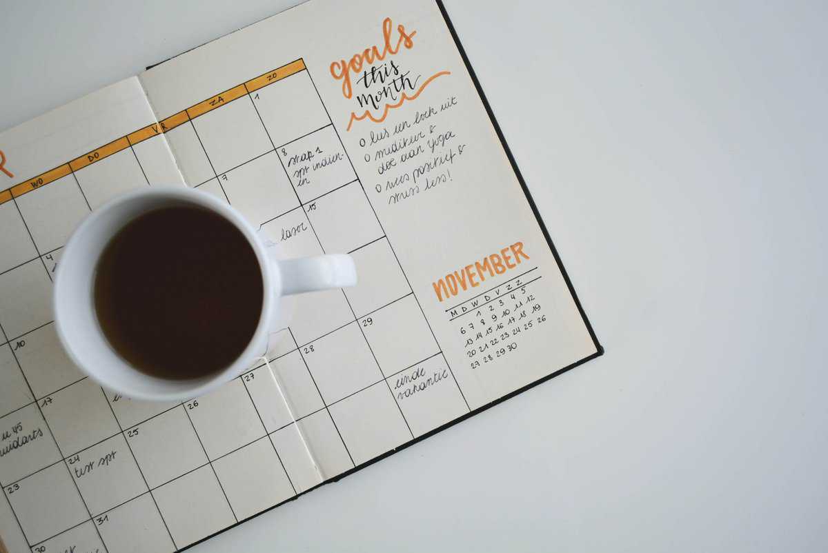 cup of coffee sitting on top of a planner calendar