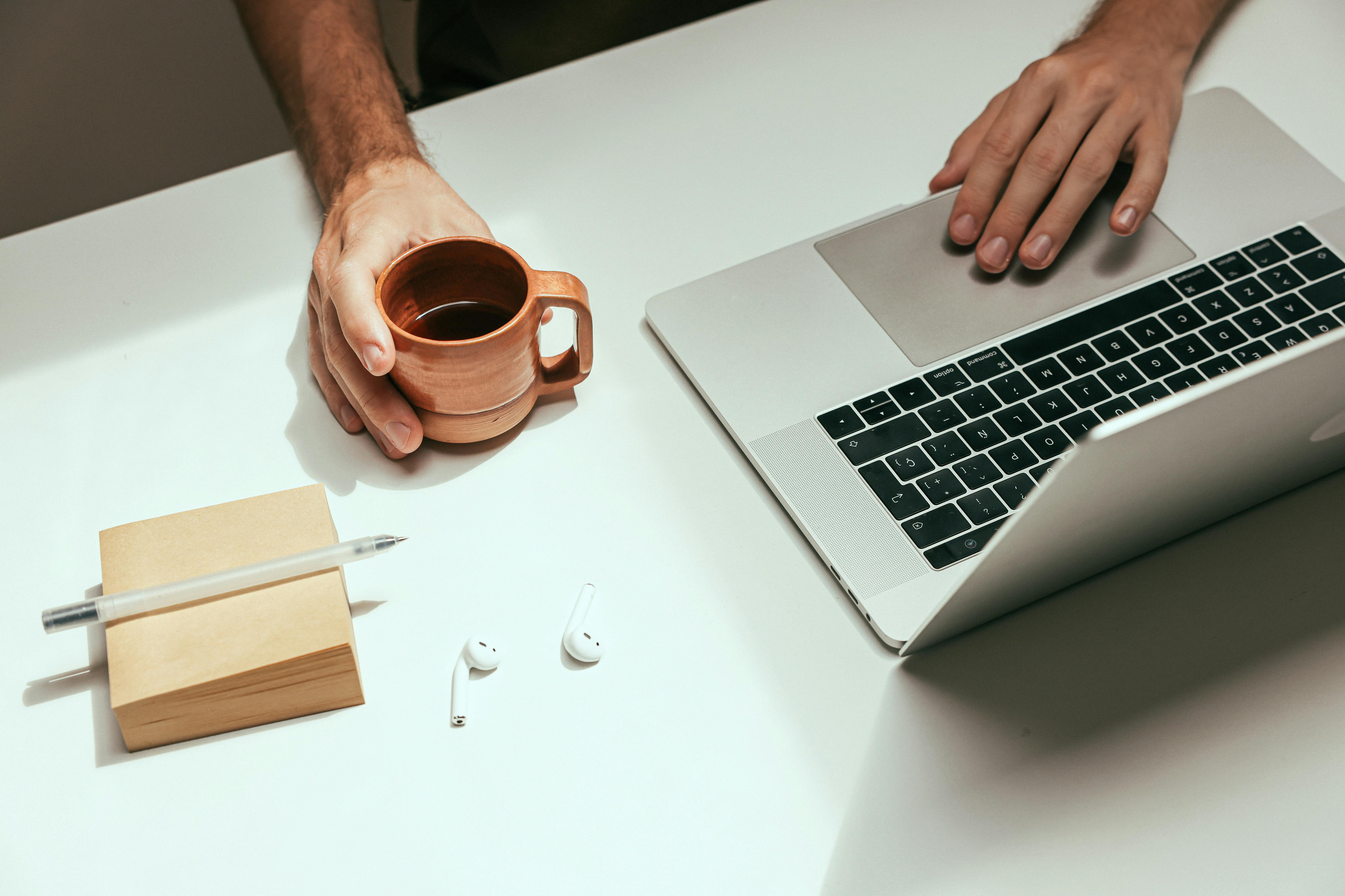 hand with cup of coffee next to keyboard